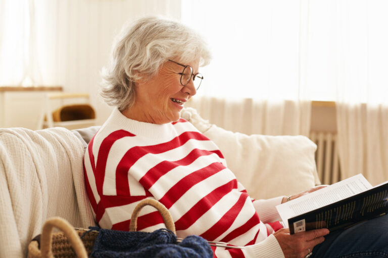 Side view of cute happy grandmother in glasses enjoying reading