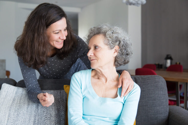 Smiling adult daughter supporting sad senior mother. Pretty young woman visiting mum in nursing home. Family concept